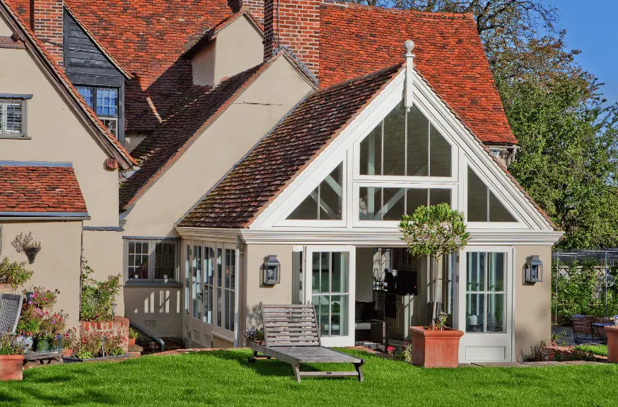 An award winning orangeries-inspired sunroom with large windows, red-tiled roof, lawn chairs, and potted plants outside.